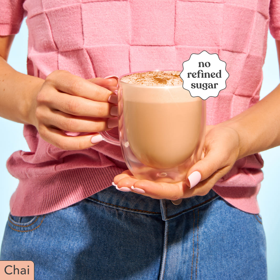 Person wearing a pink shirt and blue jeans holding a mug of Moodi Chai with 'no refined sugar' label