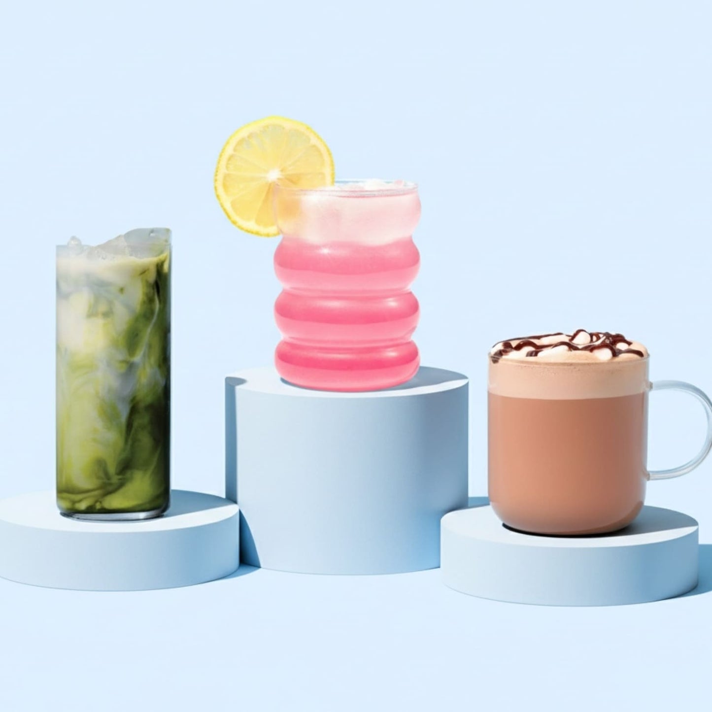 Three beverages on a blue background: pink lemonade, matcha, and hot chocolate.