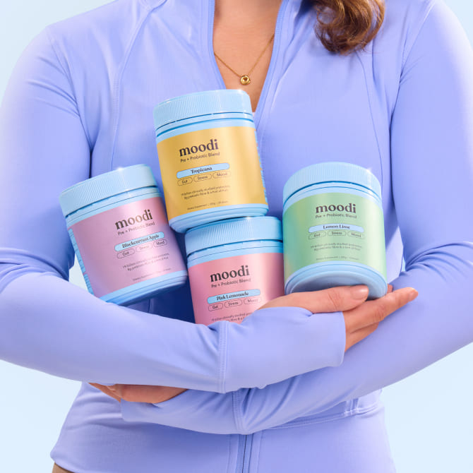 Person holding four tubs of moodi products against a light blue background