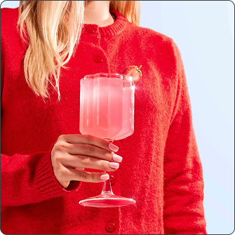 Person wearing a red sweater holding a Moodi Pink Lemonade Pre + Probiotic drink in a glass against a light blue background