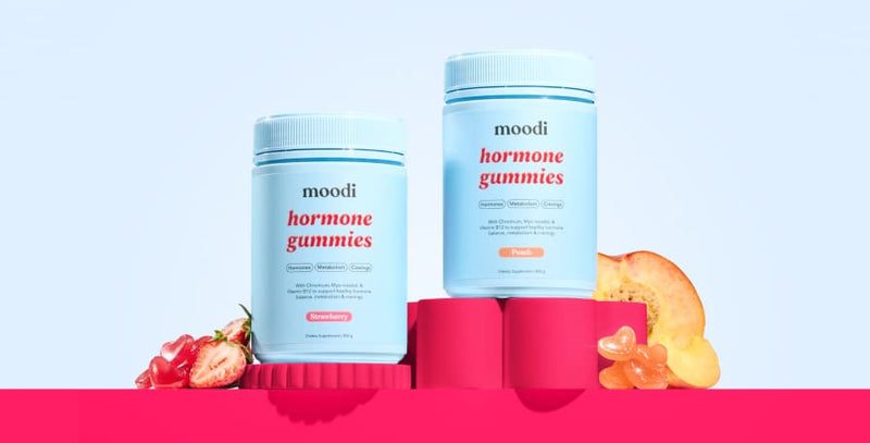 Moodi Strawberry and Peach Hormone Gummies on a red block and light blue background with gummies and fruits