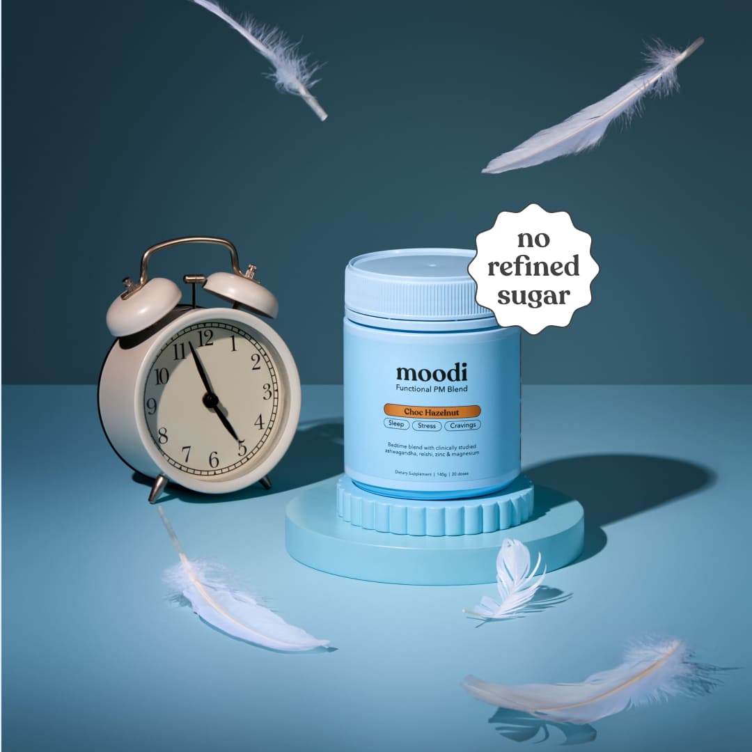 Moodi Choc Hazelnut tub with an alarm clock and feathers on a blue background