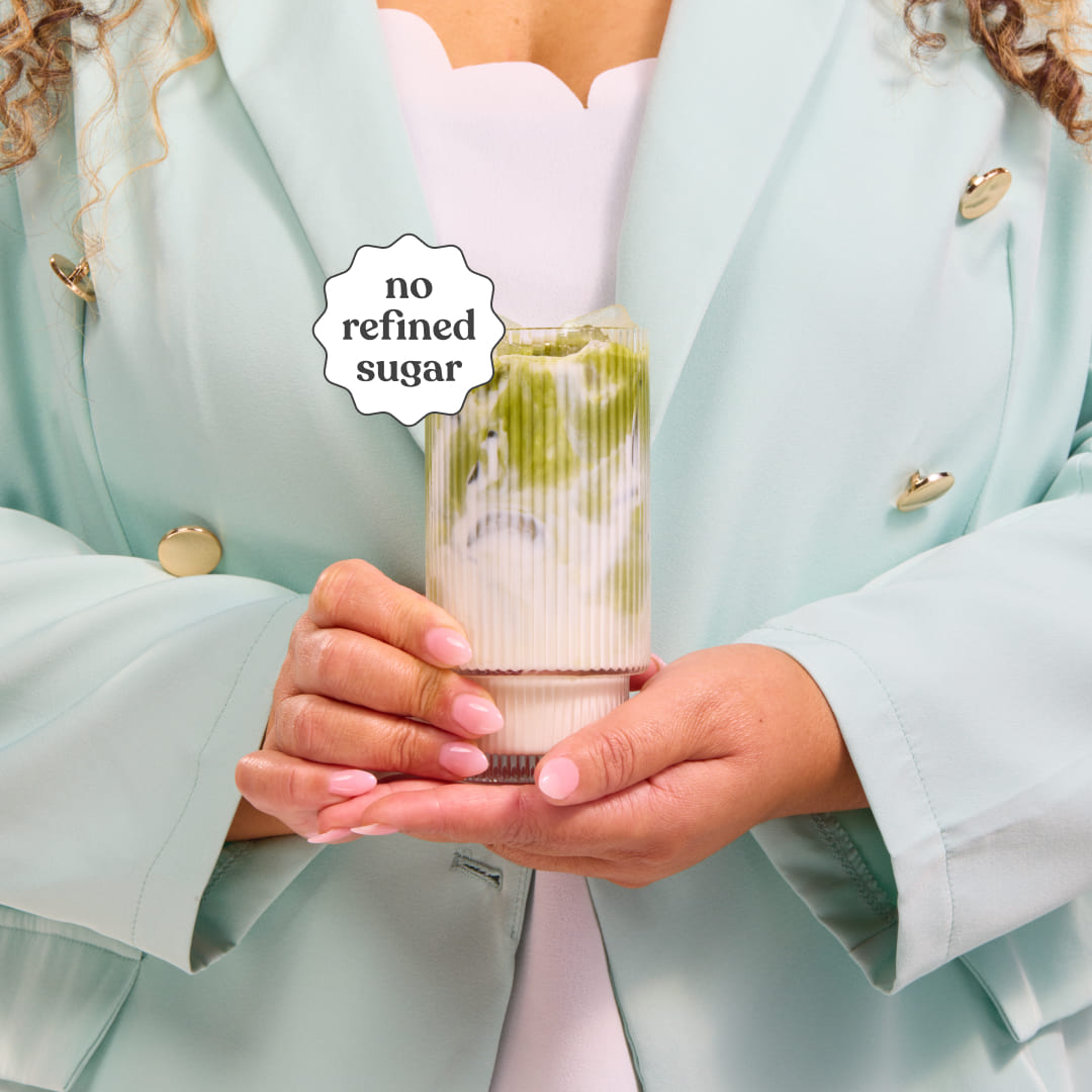 Person holding a glass of Moodi Matcha Coconut with a 'no refined sugar' label