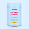 A tub of Moodi Mango Hormone Gummies against a light blue background.