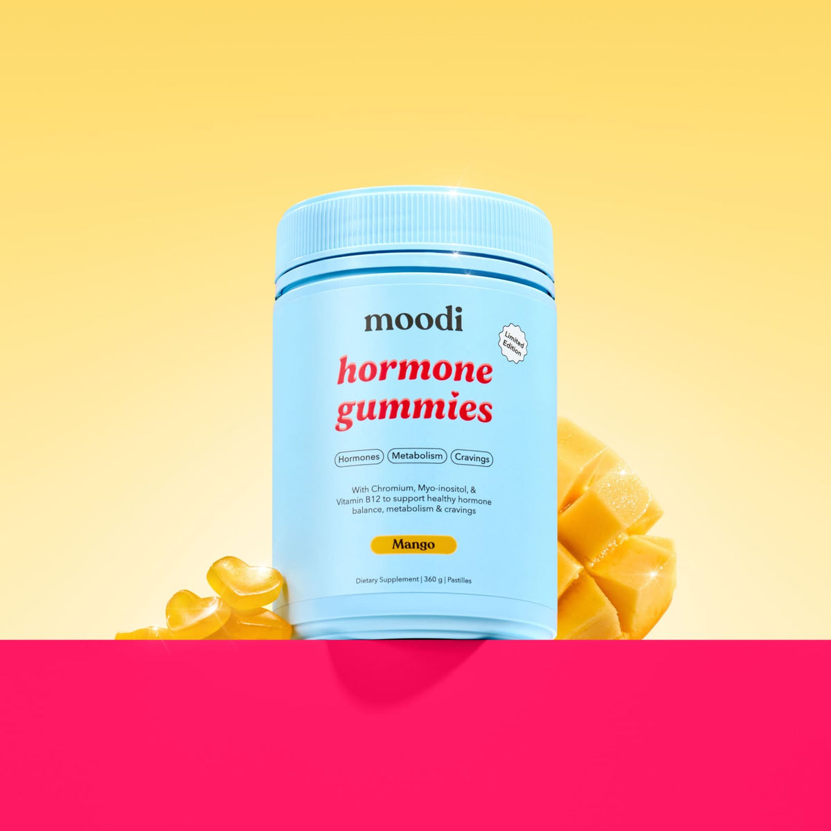 A tub of Moodi Mango Hormone Gummies centered against a yellow gradient background with stylized mango slices behind it and yellow heart gummies on the other side