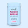Container of moodi strawbery hormone gummies on a light blue background
