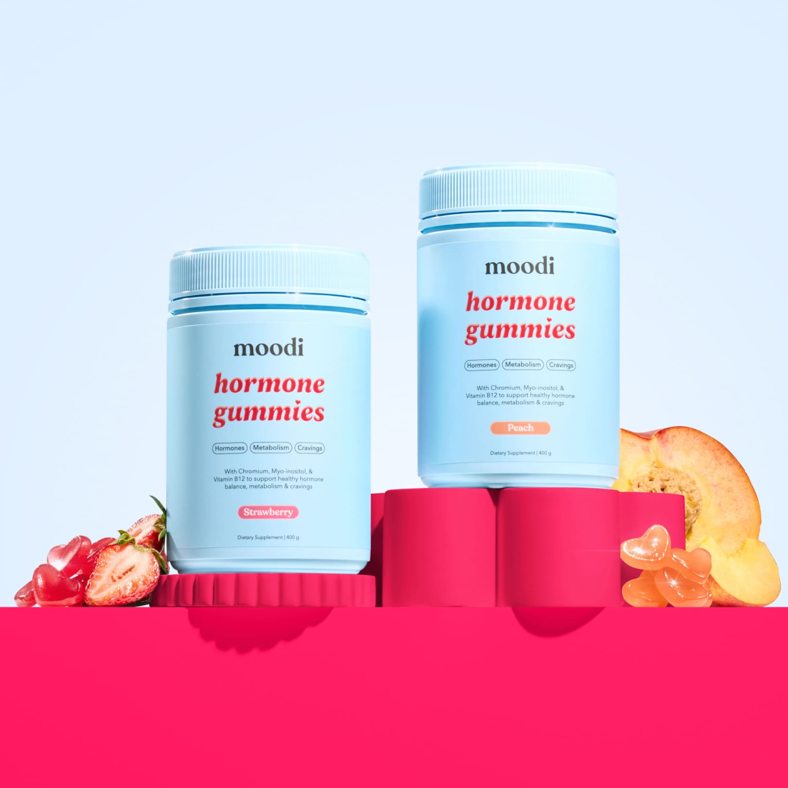 Two containers of Moodi strawberry and peach hormone gummies on a pink and blue background with fruits.