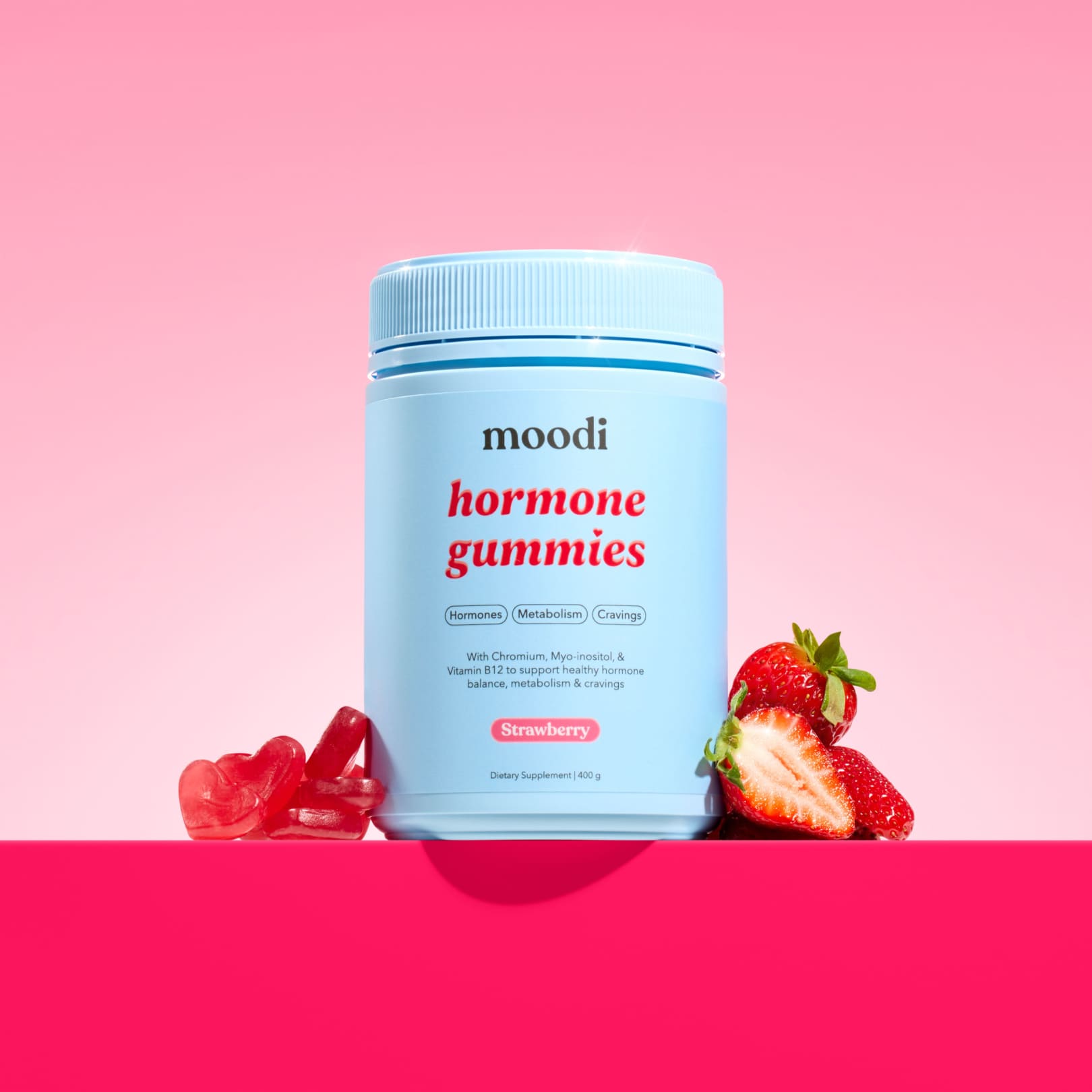 Moodi strawberry hormone gummies with strawberries and heart gummies on a pink background