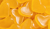 A close-up pile of translucent heart-shaped gummy candies in bright yellow-orange tones with glossy highlights.