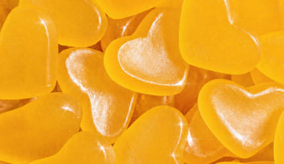 A close-up pile of translucent heart-shaped gummy candies in bright yellow-orange tones with glossy highlights.