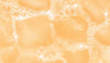 A close-up of a pale orange beverage with ice cubes and visible foam bubbles, filling the entire frame.