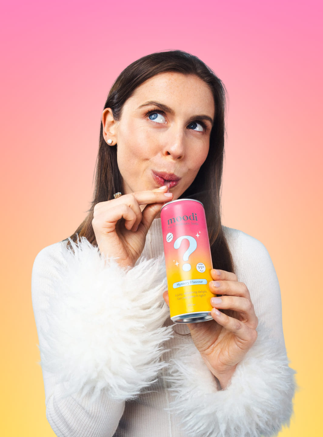 Kate in a white fluffy sweater holds and sips Mystery Flavour Pre + Probiotic Soda against a pink and yellow gradient background
